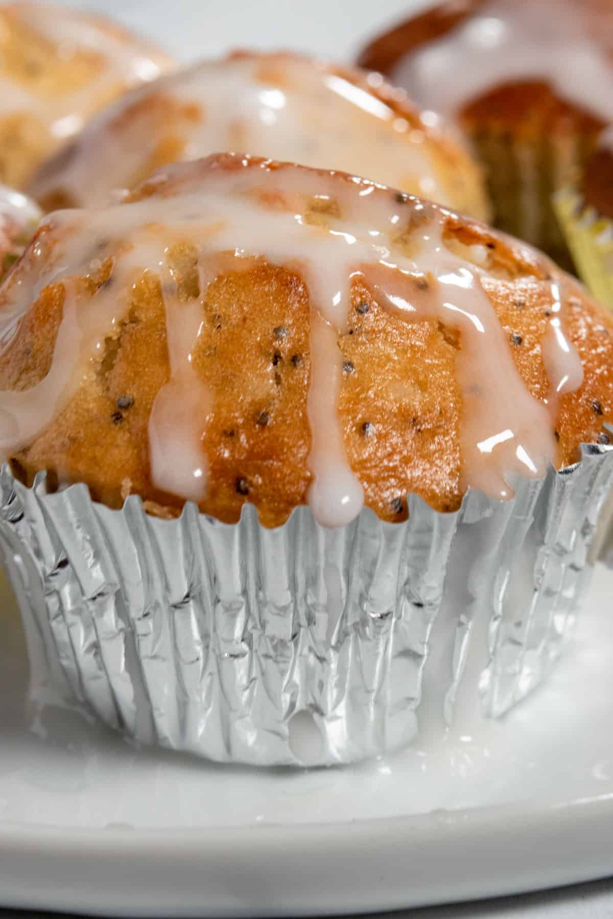 A close up shot showing a muffin sitting inside a shiny, silver cupcake liner. There are other muffins in the background. 