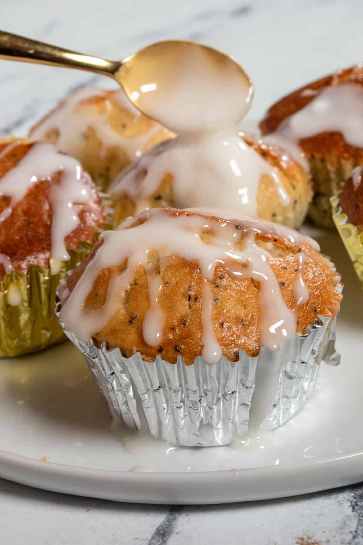 Glaze being dripped from a golden spoon onto a muffin. 