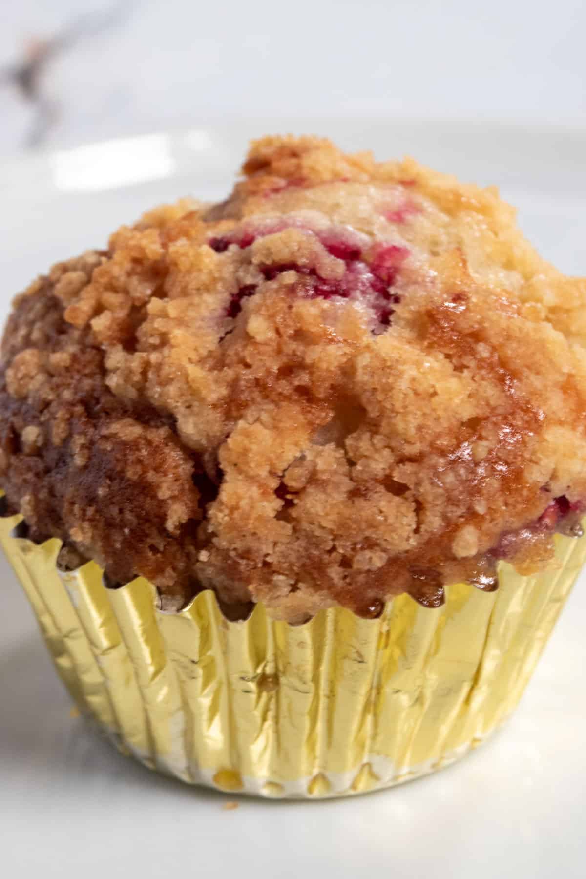 A single muffin inside a shiny golden cupcake liner. This one is erupting with hot raspberries on top. 