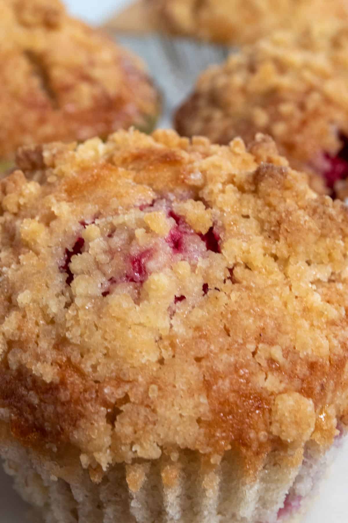 A zoomed in shot of a vegan raspberry muffin. You can see the raspberries insides which are a very deep red. The streusel on top is golden brown. 