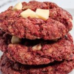 A stack of three red velvet cookies. Big chunks of white chocolate on top.