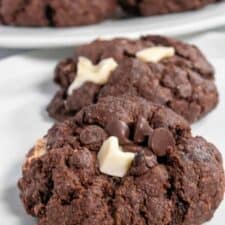 Two of my vegan triple chocolate cookies on a shiny white plate. Both dark chocolate and white chocolate chips on top.