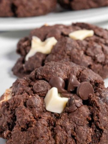 Two of my vegan triple chocolate cookies on a shiny white plate. Both dark chocolate and white chocolate chips on top.