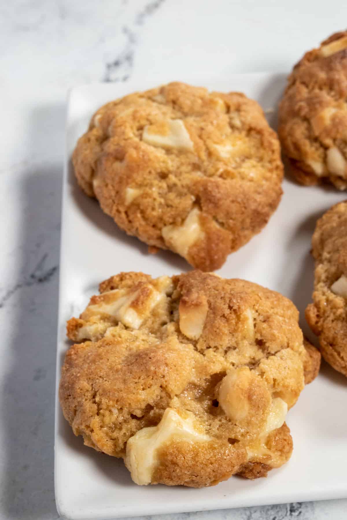 Two melty vegan white chocolate macadamia cookies on a white plate. 