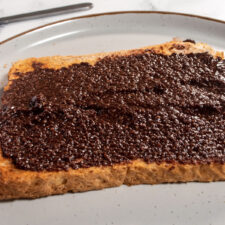 Vegan brownie batter spread onto a slice of toast on a round plate.