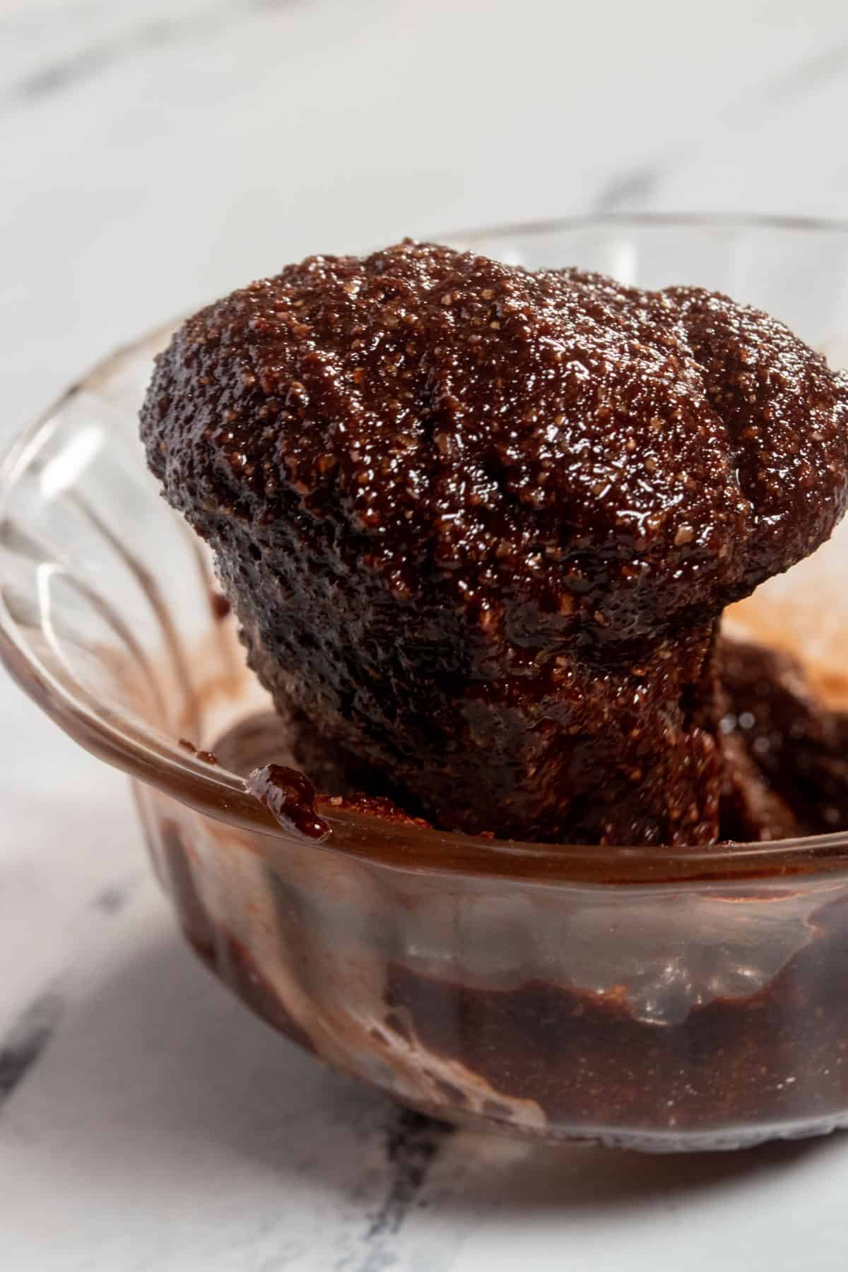 Brownie batter being spooned into a glass bowl. It is thick in consistency as it drips from the spoon. 