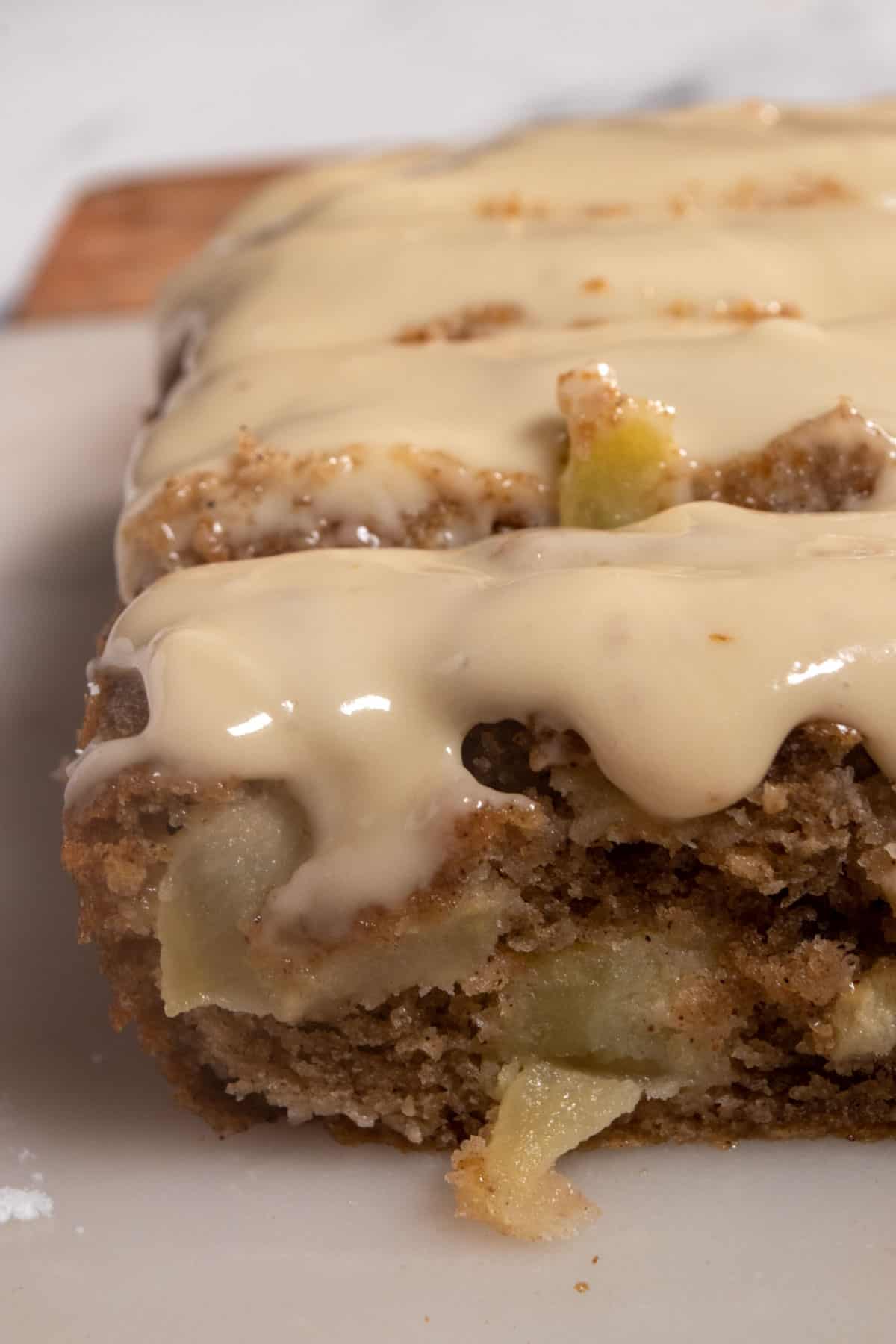 A whole loaf of my vegan apple cinnamon cake on a marble platter. Maple glaze is dripping down the front. 