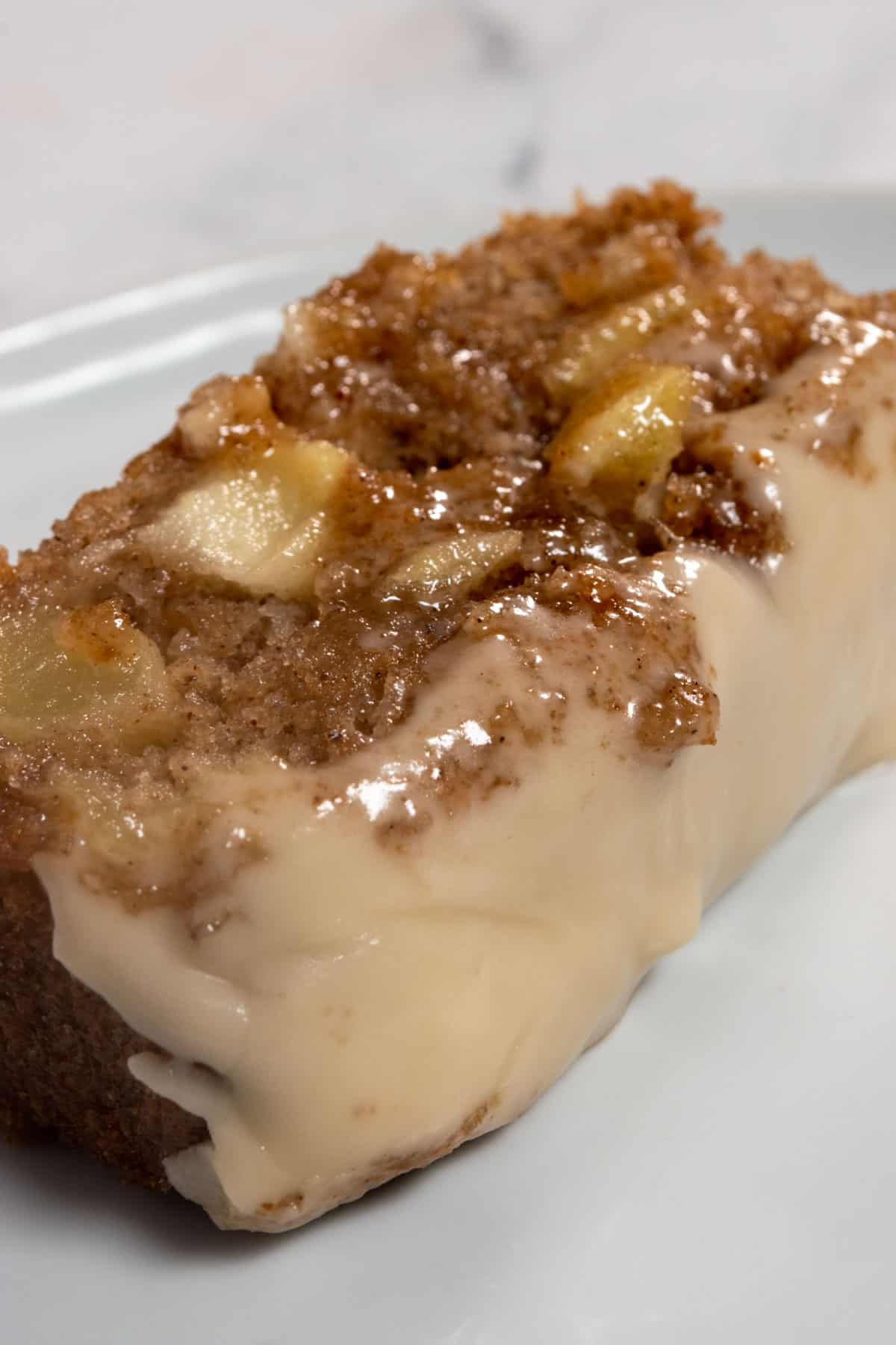 A large, moist slice of my vegan apple cinnamon cake on a white plate. The apples inside are golden. 