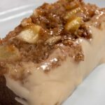 A thick slice of vegan apple cinnamon cake on a shiny, white plate. It is very moist and topped with maple glaze.