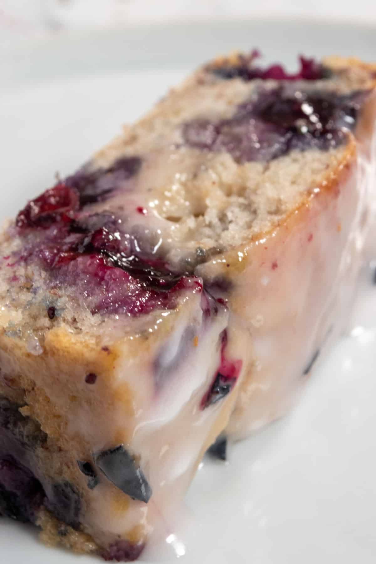 A thick slice of my vegan blueberry banana cake. The blueberries inside have burst and are bright purple.