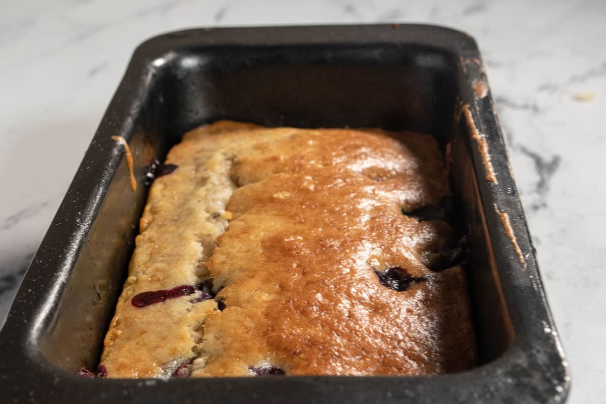 A golden brown, baked loaf cake inside its tin cooling. 