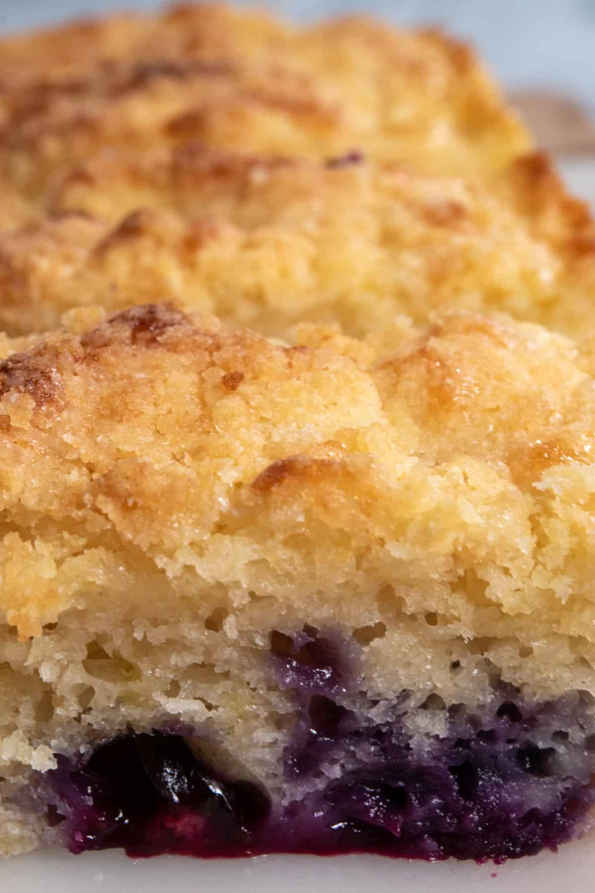 A super close up shot of my vegan blueberry lemon cake. It looks golden and the warm blueberries are bright purple and dripping. 