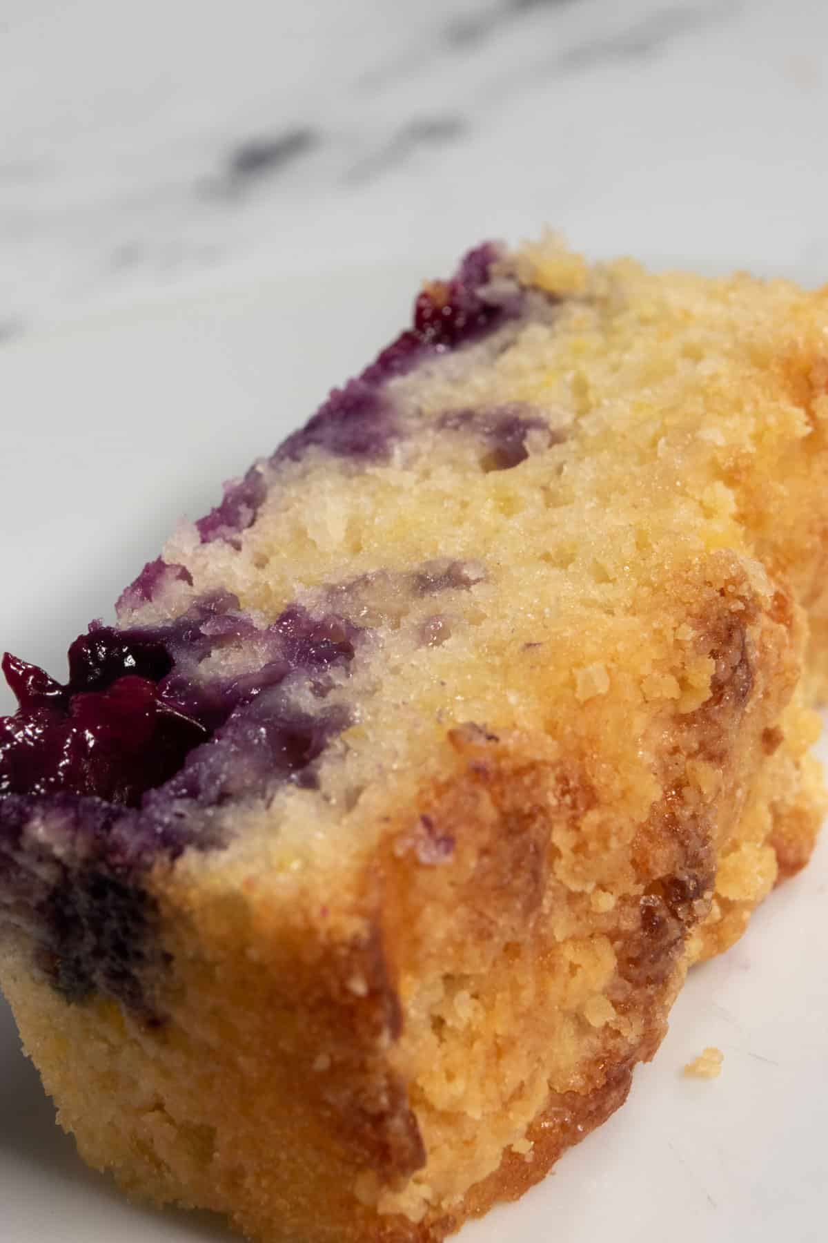 A large, thick slice of my blueberry lemon cake. It has a glimmer to it and it is full of blueberries. 