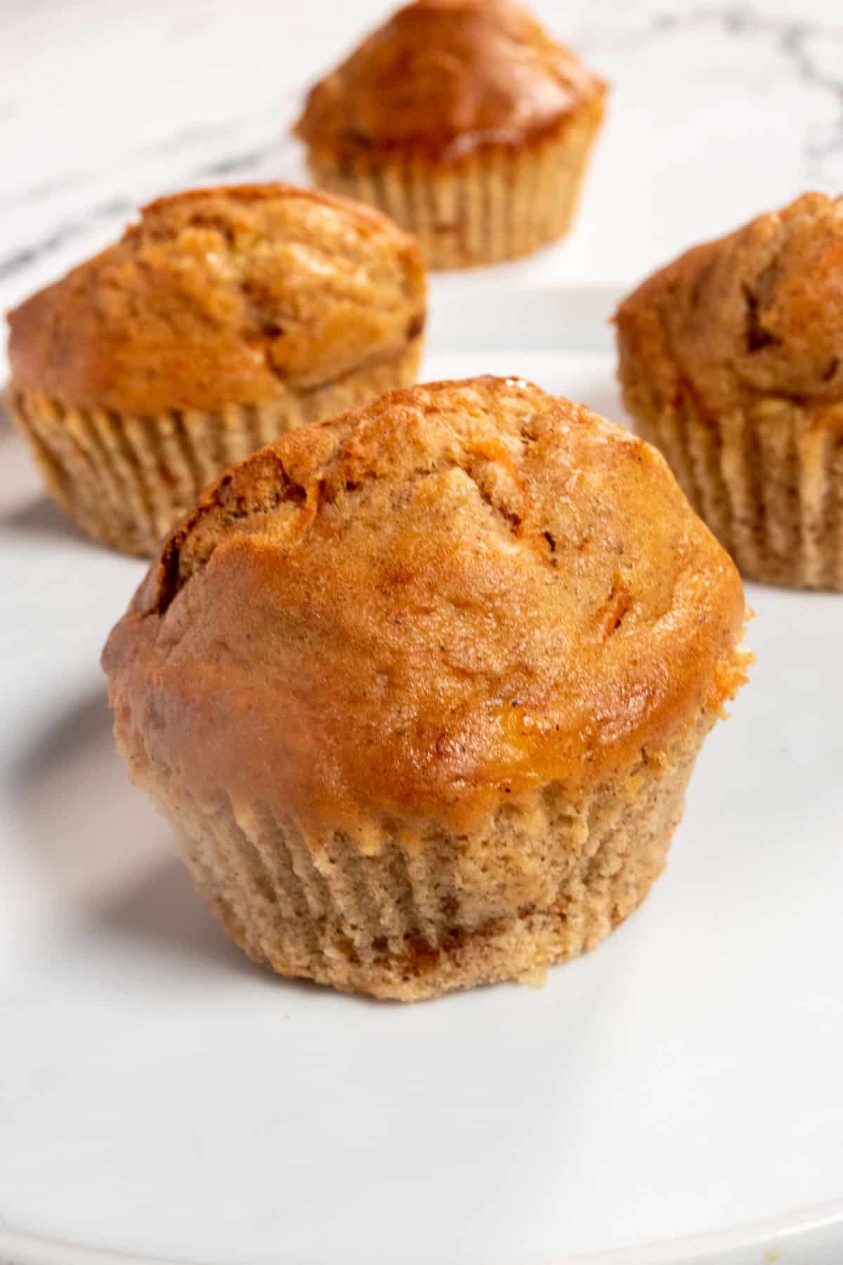 Three golden vegan carrot cake muffins on a white plate. They are not glazed yet. 