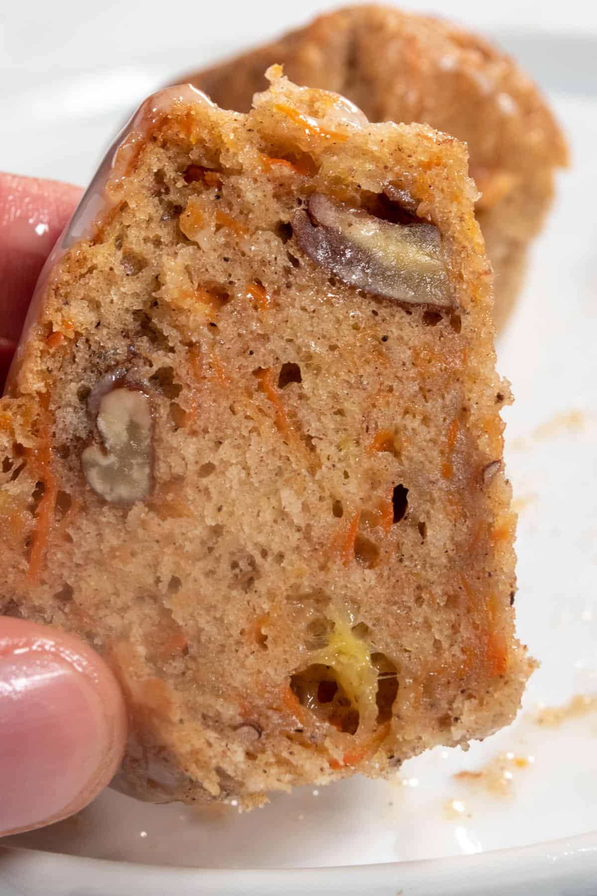 The insides of a muffin being shown close up to the camera. Lots of chopped pecans inside. 
