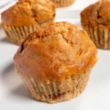 Three vegan carrot cake muffins on a white plate. They are golden in colour.