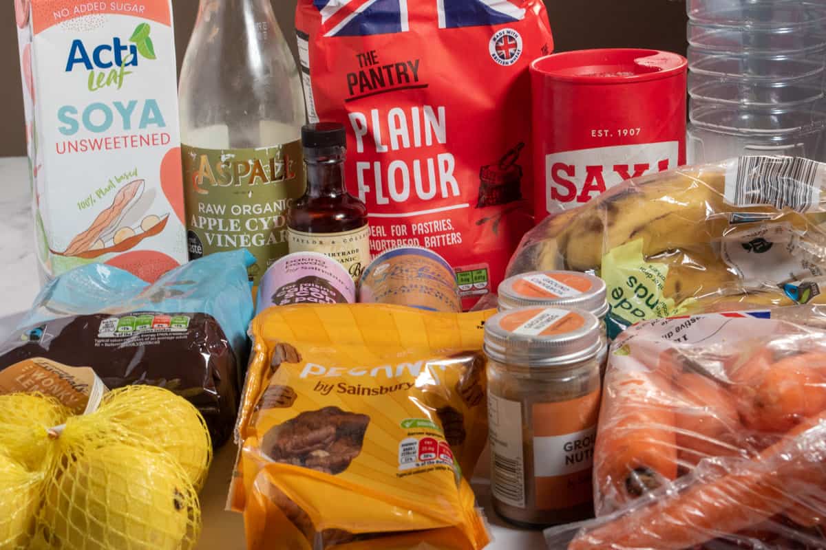 The ingredients which are needed to make vegan carrot cake muffins laid out in front of a brown wall.