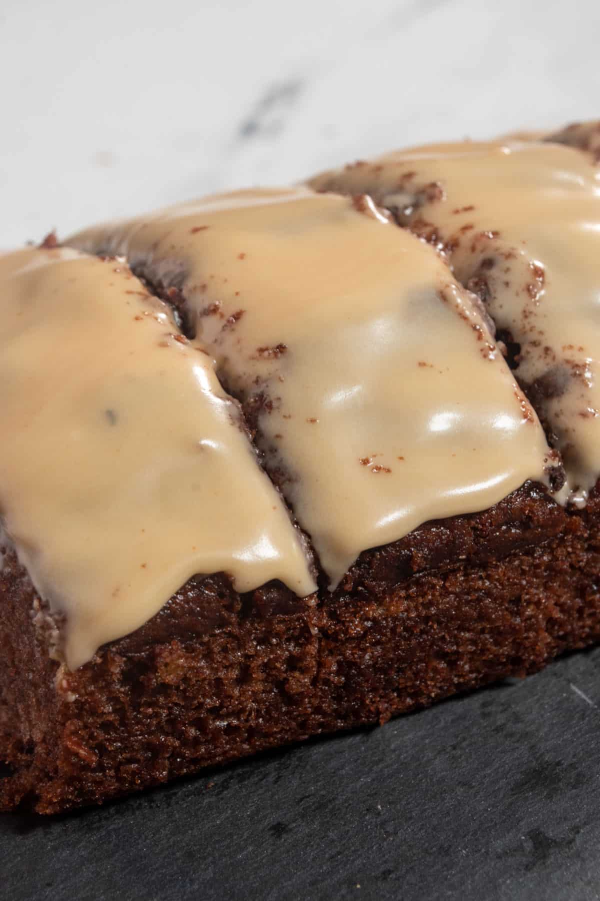 Three thick slices of vegan chocolate banana bread topped with a layer of Biscoff glaze on top. It sits on a slate board.