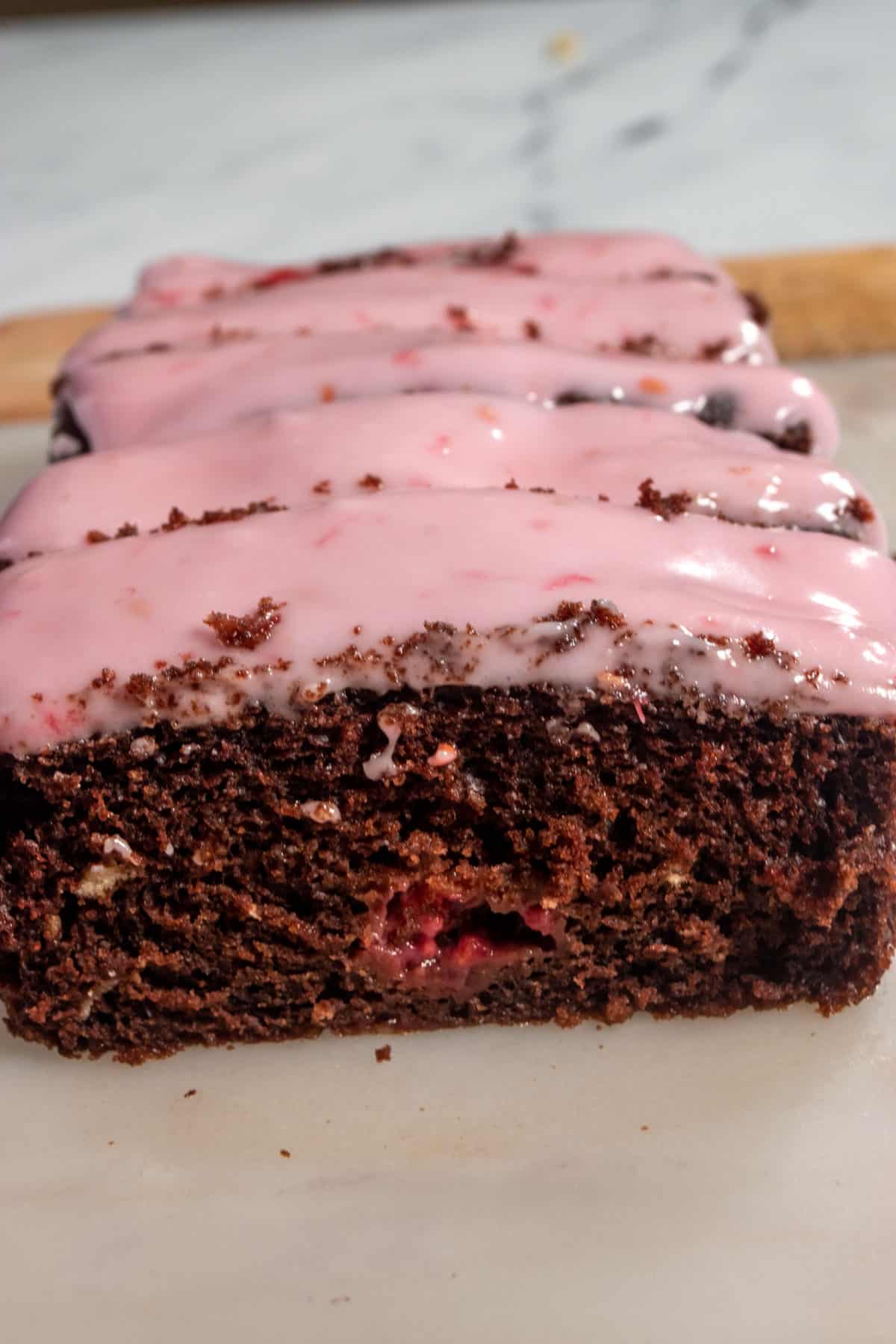 A whole loaf of my vegan chocolate raspberry cake. There are raspberries inside the cake and lots of pink glaze on top.  