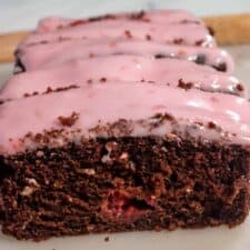 A whole loaf of my vegan chocolate raspberry cake. There is a bright pink glaze on top and raspberries inside the cake too.