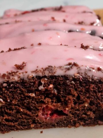 A whole loaf of my vegan chocolate raspberry cake. There is a bright pink glaze on top and raspberries inside the cake too.