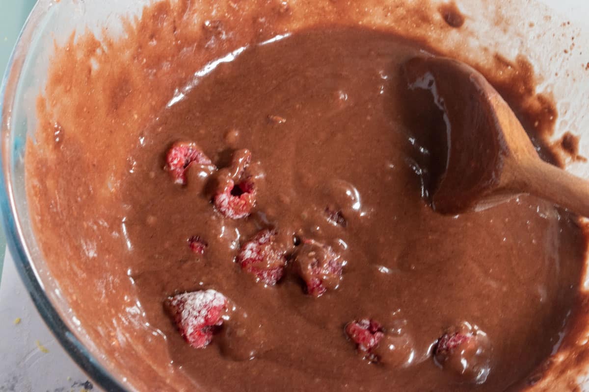 The dry and wet ingredients have been folded together inside the bowl creating a creamy, chocolatey batter. The fresh raspberries have also been added. 