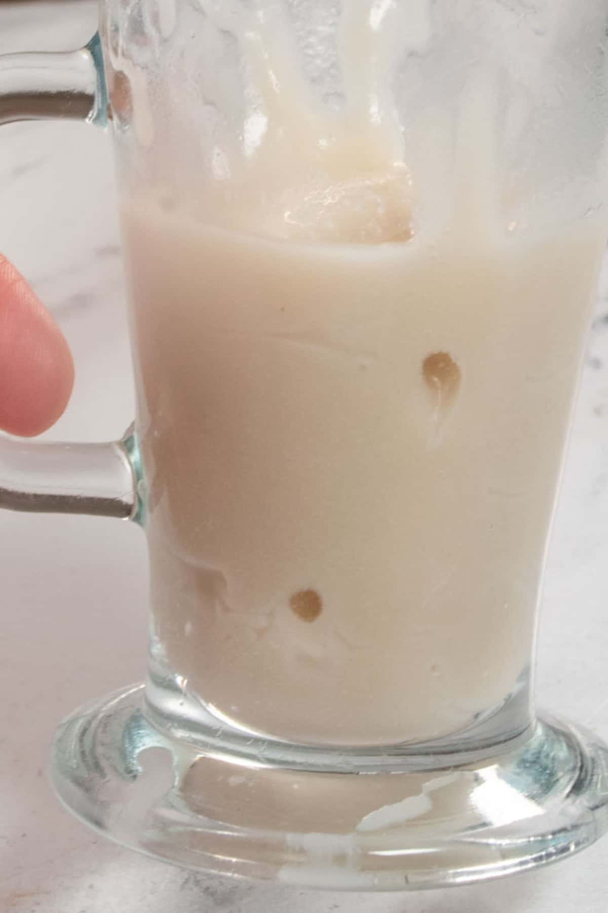 A hand holding a tall glass filled with vegan condensed milk. 
