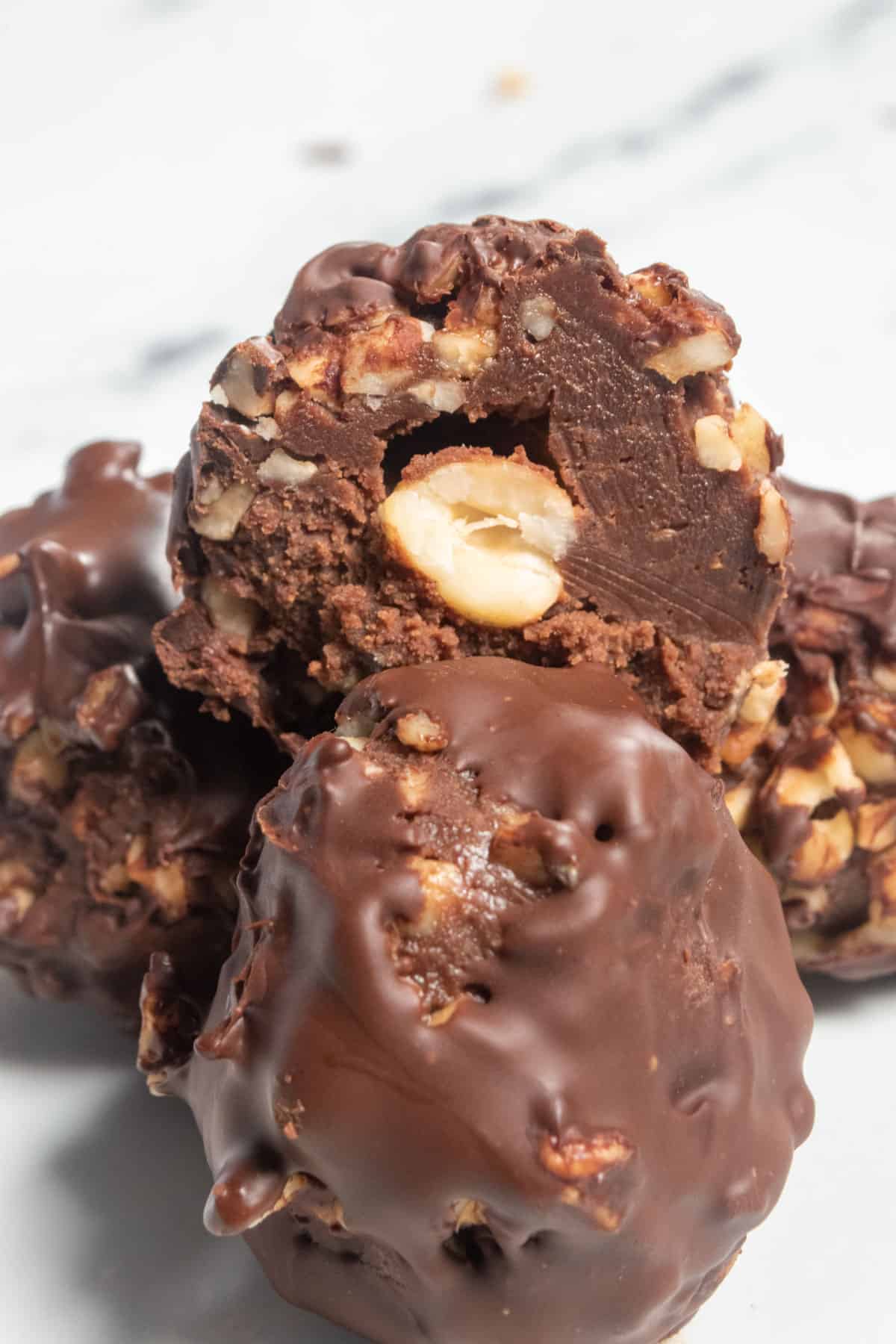 A stack of vegan ferrero rocher truffles. The one on top is sliced in half. There is a whole hazelnut kernal in the middle. 