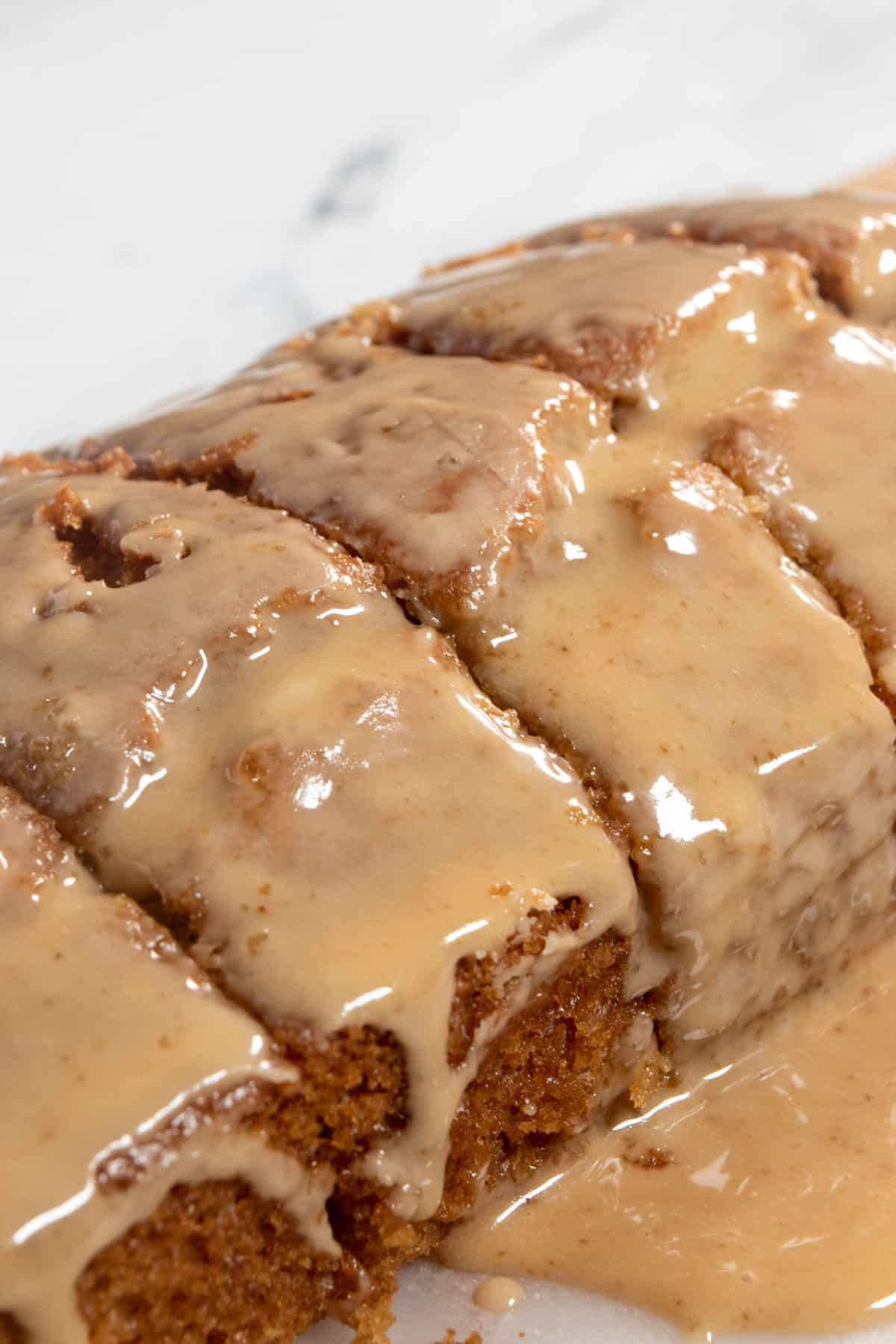 A whole vegan ginger cake loaf with coffee glaze generously poured over it. The glaze is dripping down the sides and the loaf is sliced into five equal pieces.