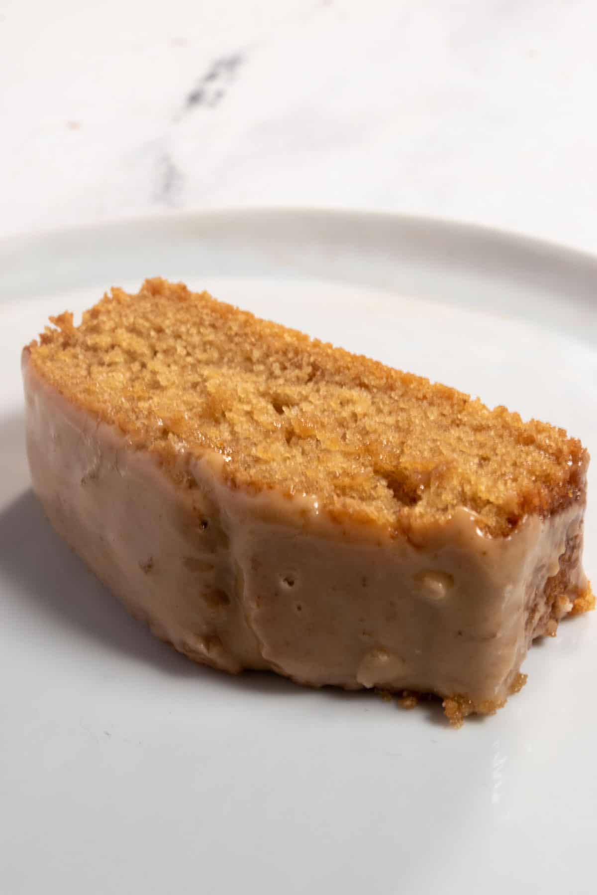 A single, thick slice of my vegan ginger cake laying flat on a white plate. It is moist and golden. 