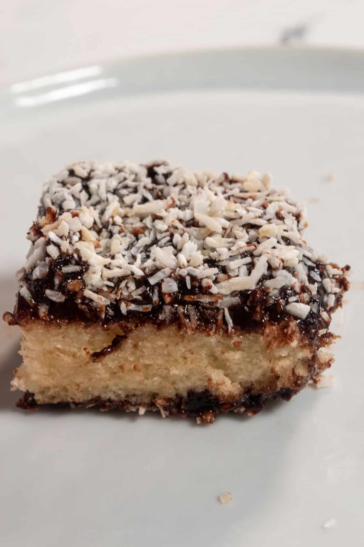 A sliced vegan Lamington bar. You can see the vanilla cake inside. There's lots of coconut on top of the melty chocolate coating.