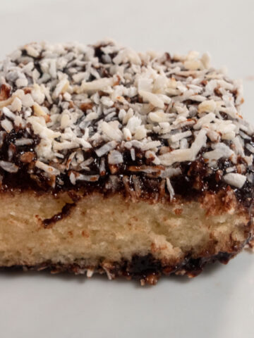 A single slice of vegan lamington cake. It has been sliced open and coconut has been sprinkled on top generously.