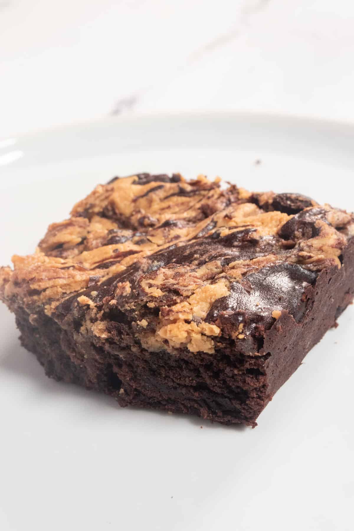 A side-angled photo of a fudgy brownie on a white plate. 