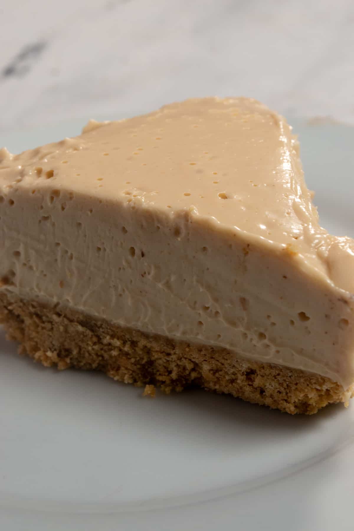 A large slice of my vegan peanut butter cheesecake on a small, white saucer. This slice hasn't been decorated with the chocolate topping.
