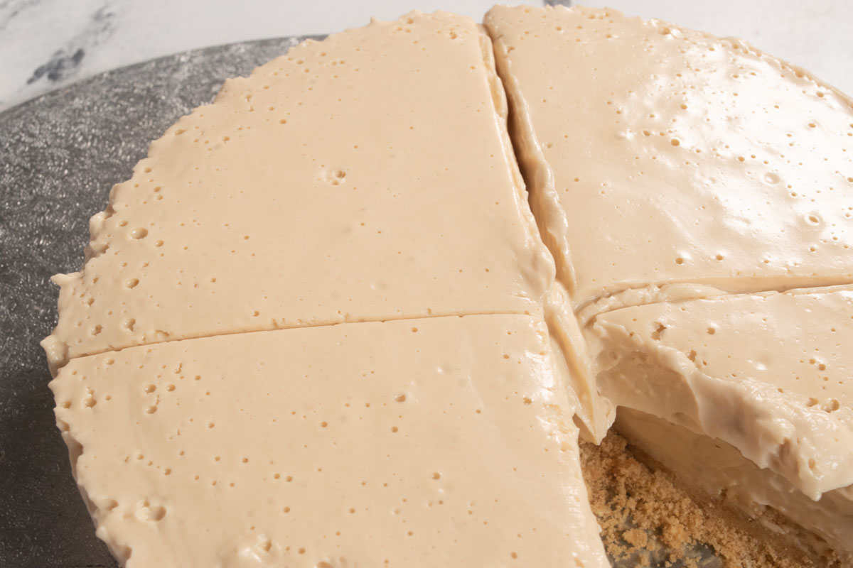 The vegan peanut butter cheesecake has been chilled and has thickened. This image shows an aerial shot of a whole cheesecake with a small slice missing.