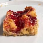 A single slice of vegan pudding cake. Lots of raspberry jam spread on top.