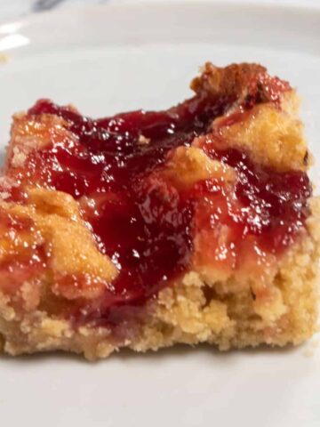 A single slice of vegan pudding cake. Lots of raspberry jam spread on top.