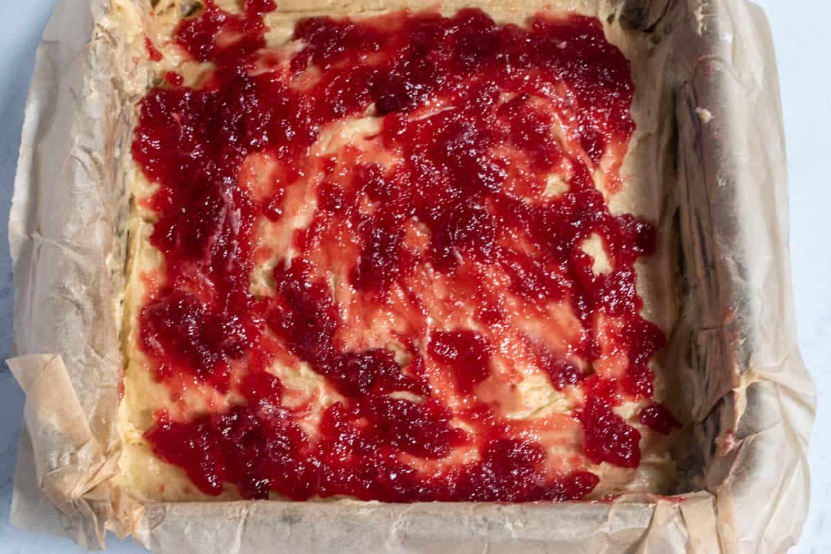 Raspberry jam has been spread on top of the batter. It is covered generously. 