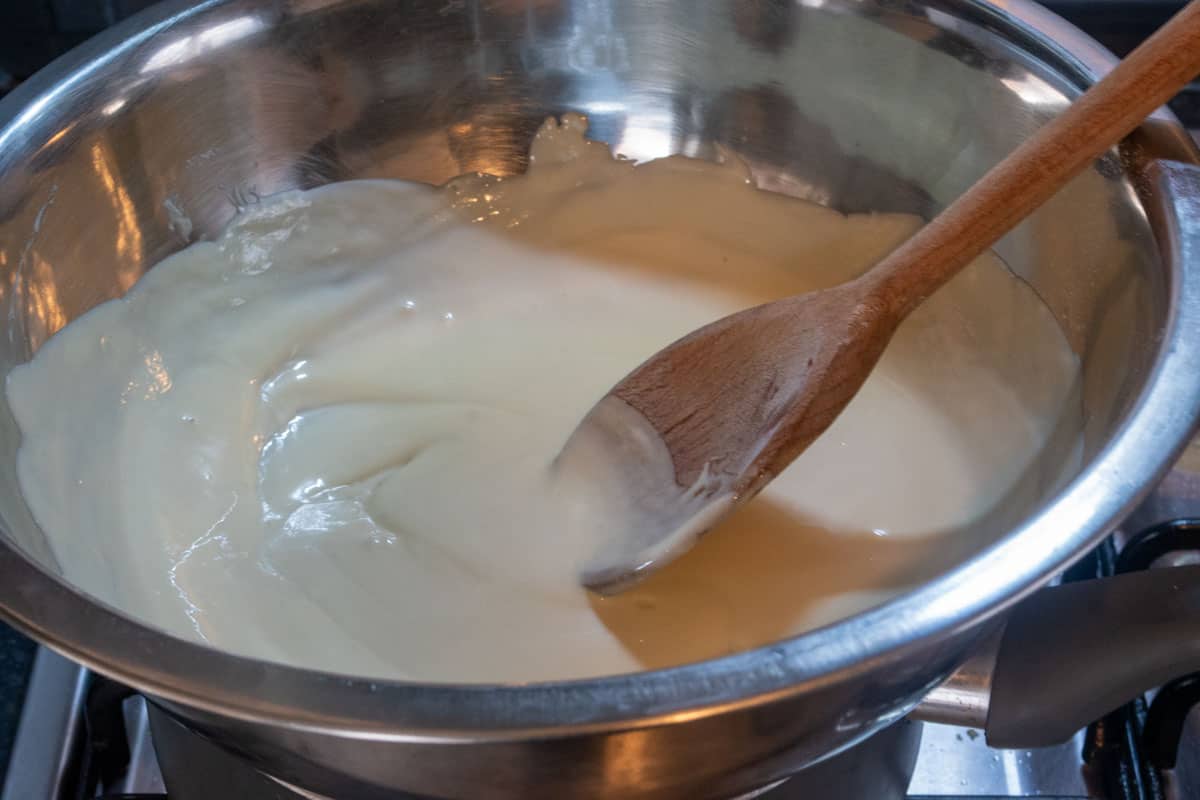 The vegan white chocolate being melted inside a heatproof bowl over boiling water. 