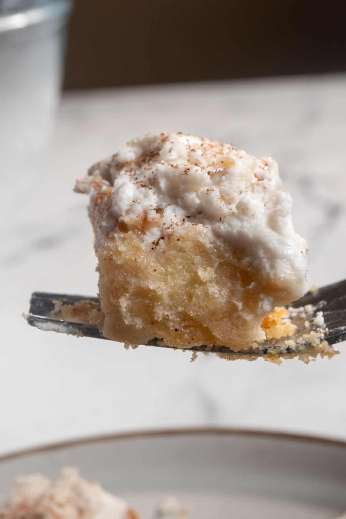 A smaller, moist slice of vegan tres leches cake being held to the camera lens on a fork. 
