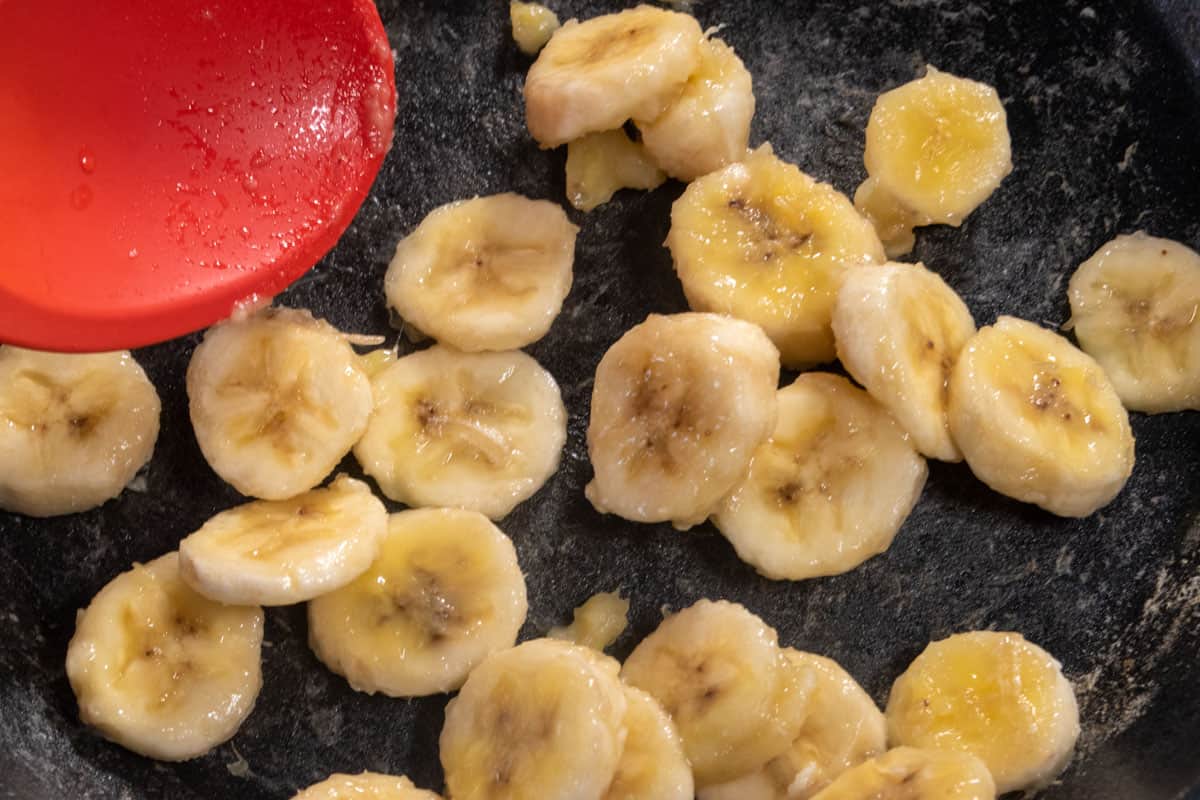 Bananas inside a black frying pan being stirred over the heat. 