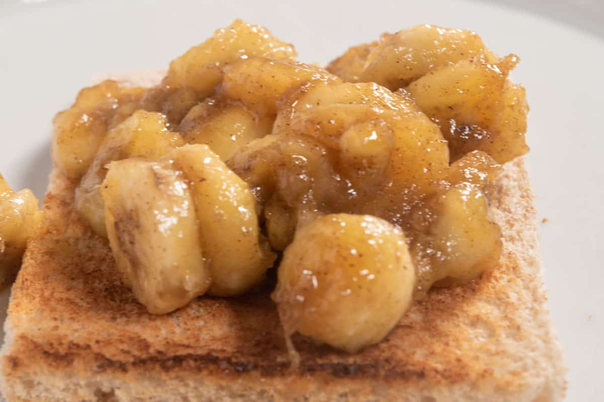 The cooked banana slices have been poured over a slice of toast. 