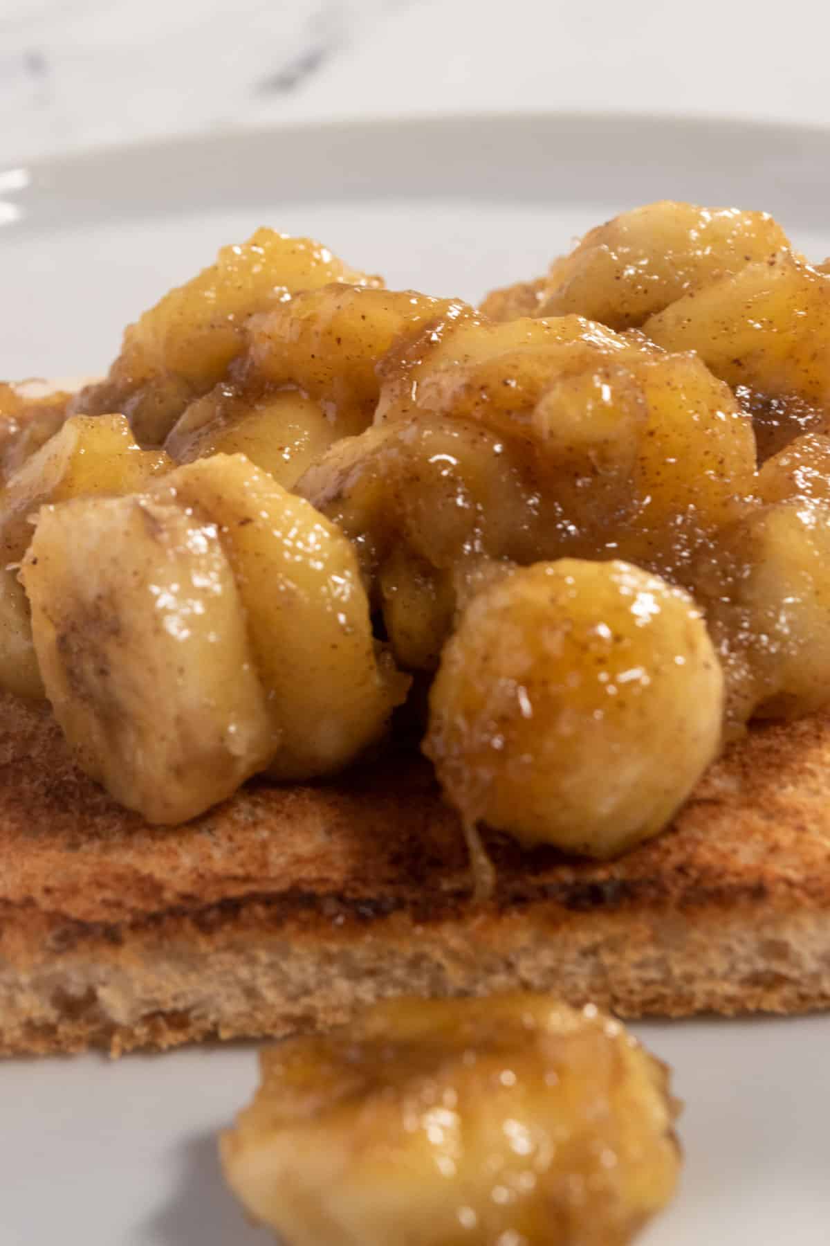 Golden brown banana chunks on a single slice of wholemeal bread. One has fallen off onto the white plate. 