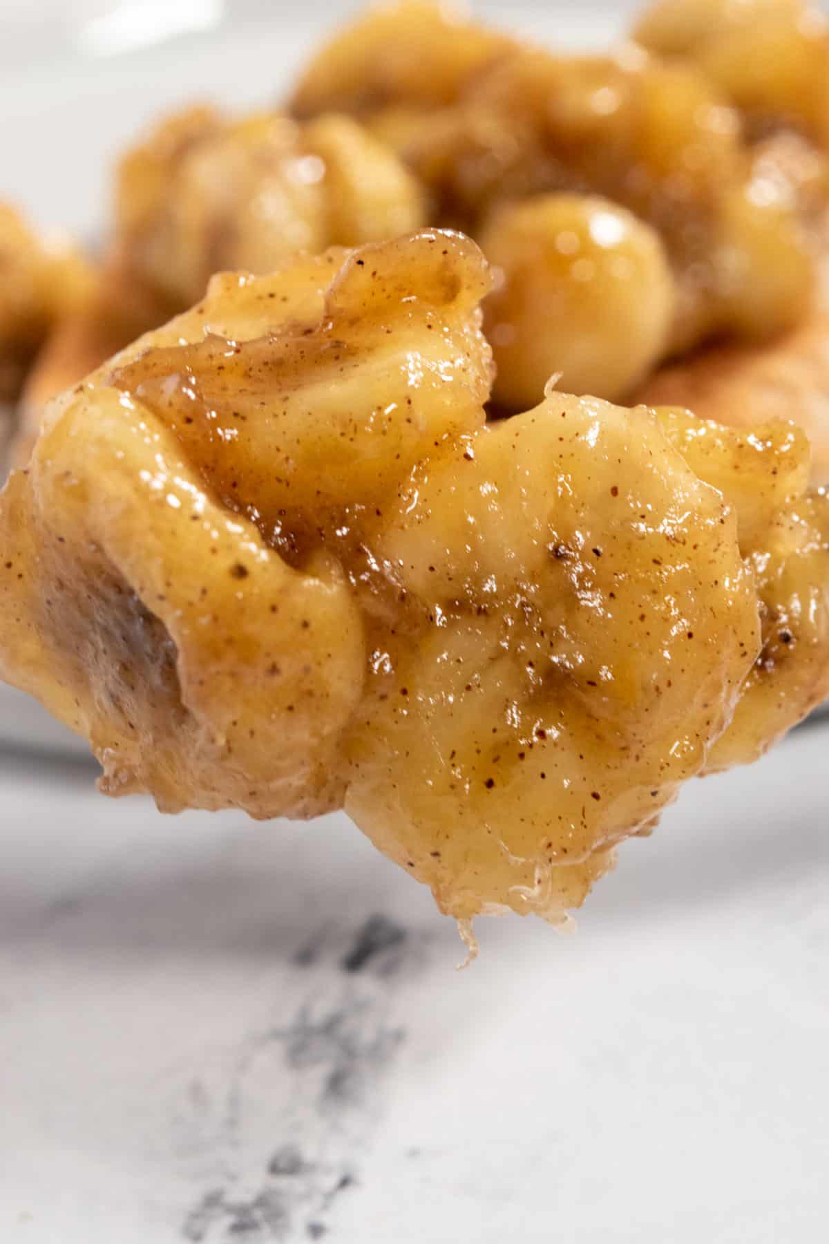 A spoonful of the bananas being held up in the air. They are golden and more caramelized bananas sit in the background.