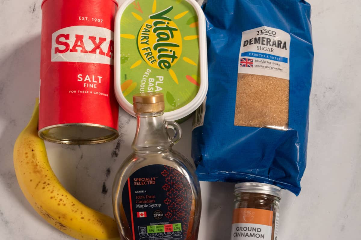 The six ingredients that you will need to make my caramelized bananas recipe laid out neatly over a white, marble background.