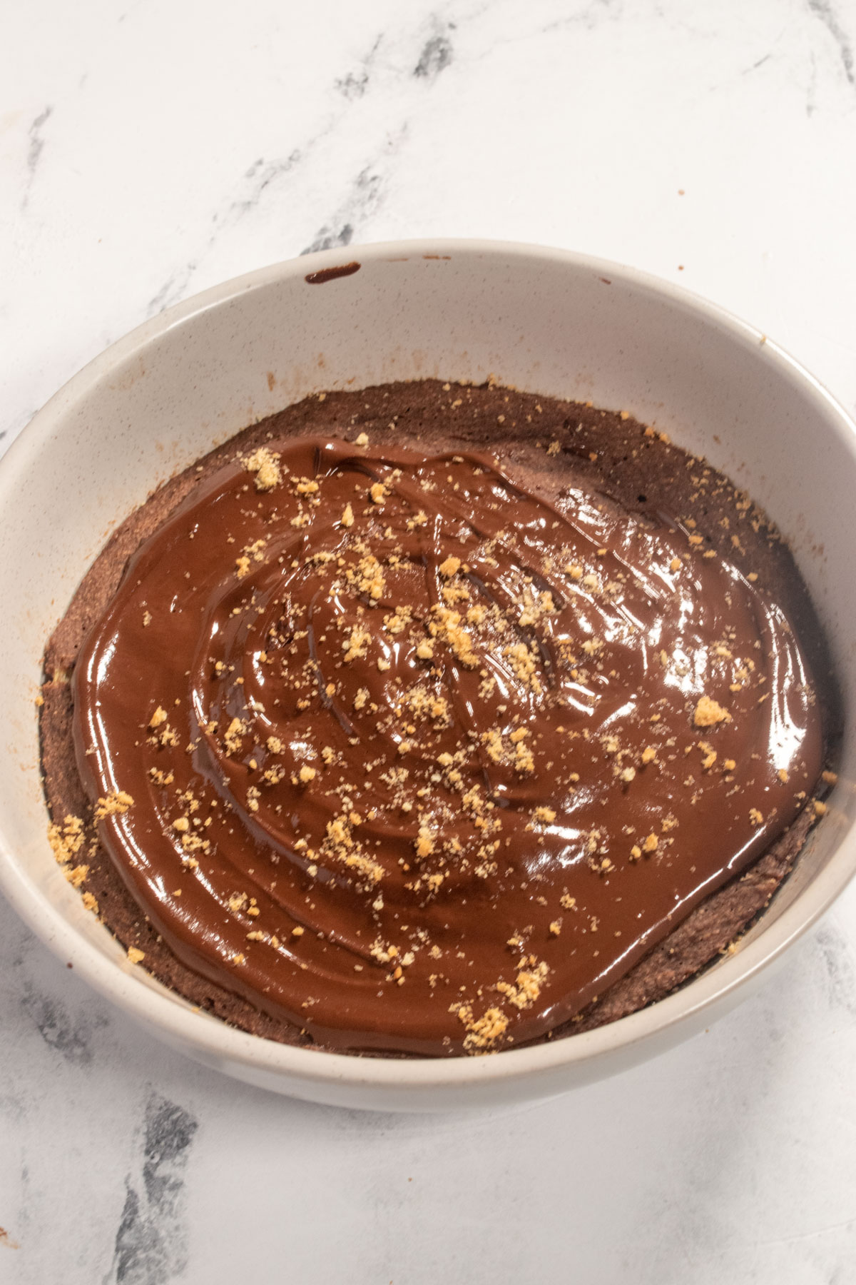 A large portion of oatmeal inside a light grey bowl. The chocolate is spread smoothly on the oats and is very shiny. 