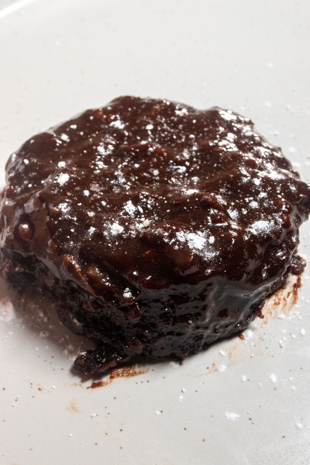 A zoomed in photo whole chocolate mug cake on a white plate. The top of the cake is melted and runny. 