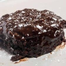 A close up photo of a single, melty chocolate chip mug cake on a white plate. It is topped with powdered sugar.