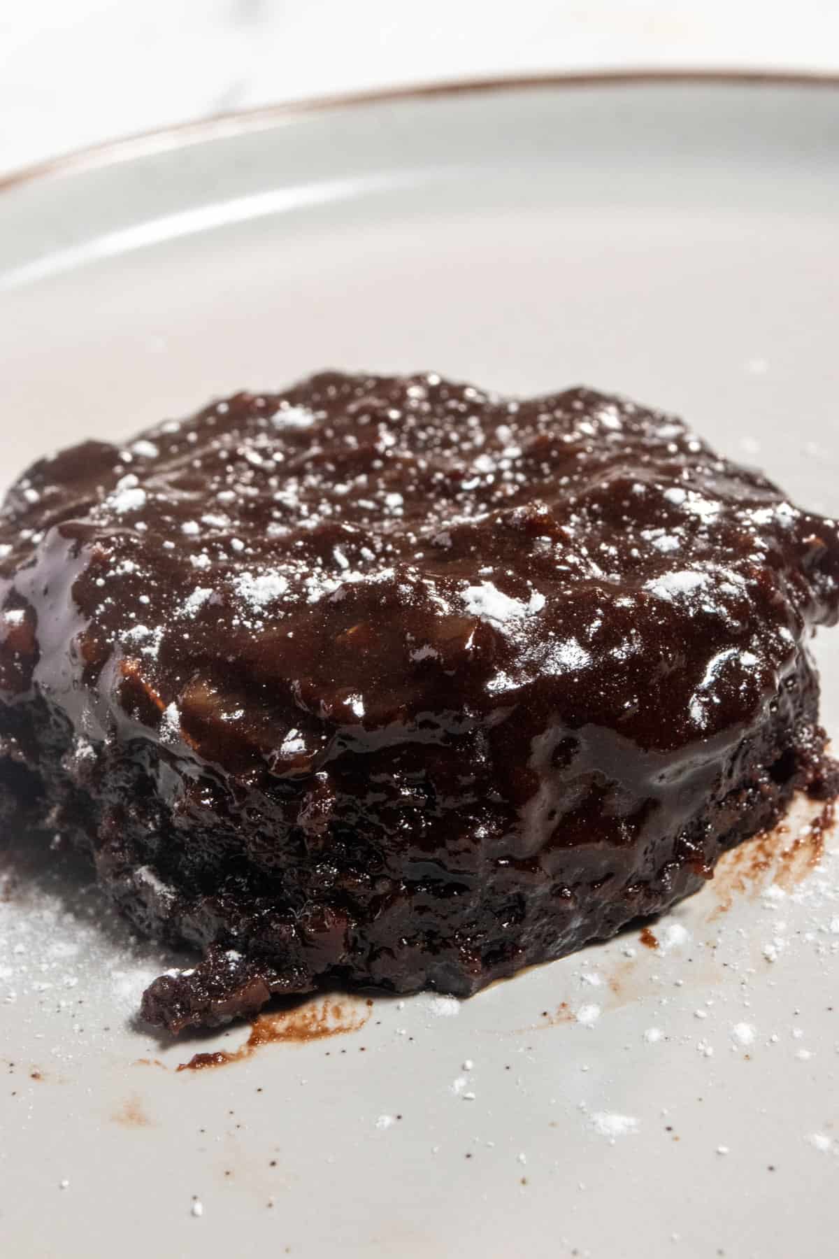 A whole chocolate chip mug cake. It's sitting on a brown-rimmed white plate. The chocolate on top is melty and topped with powdered sugar. 