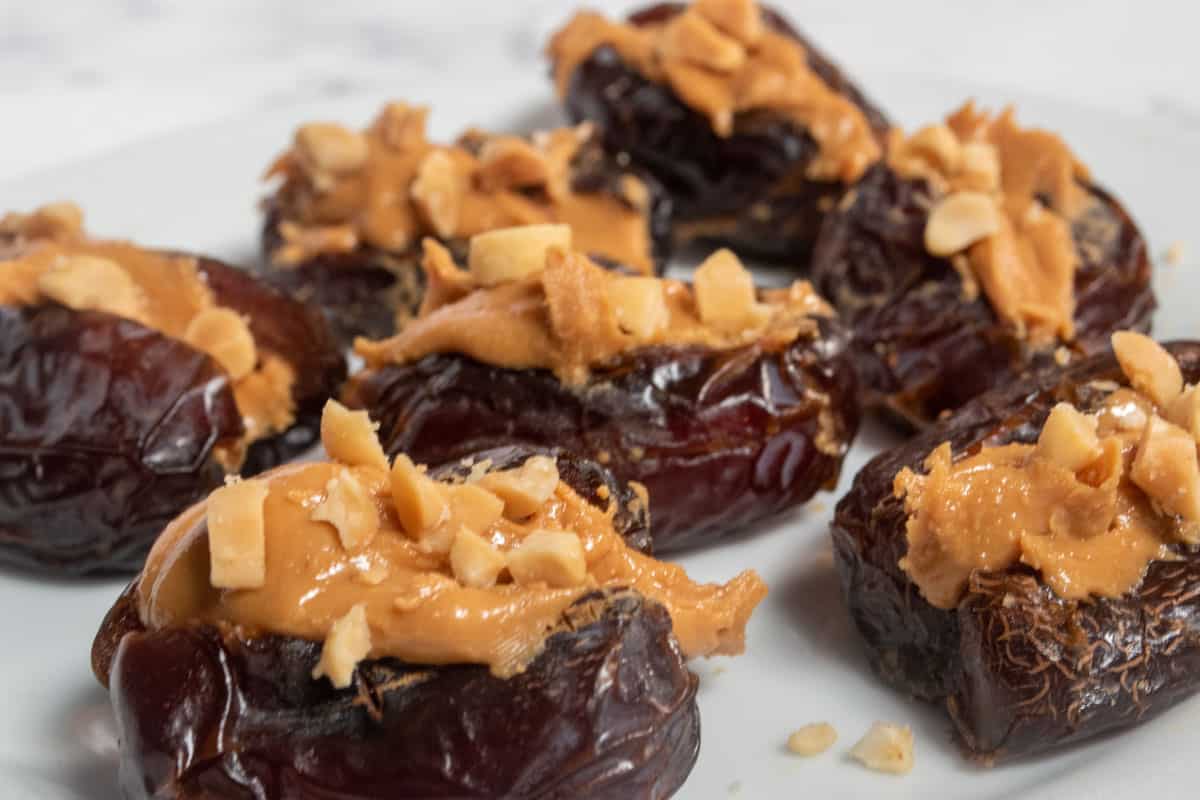 Many peanut butter stuffed dates on a large, white plate. They haven't been decorated with peanuts or chocolate yet. 